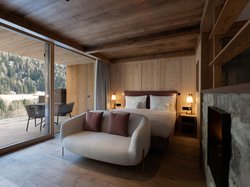 Hotel Latemar mit Dolomitenblick Schlafzimmer aus Holz mit Sofa, Doppelbett und Blick auf den Wald