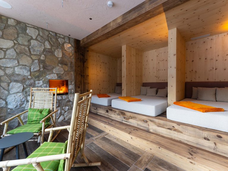 Hotel Latemar mit Dolomitenblick Entspannungsbereich mit Holzbettchen, brennendem Kamin und grünen Sitzkissen