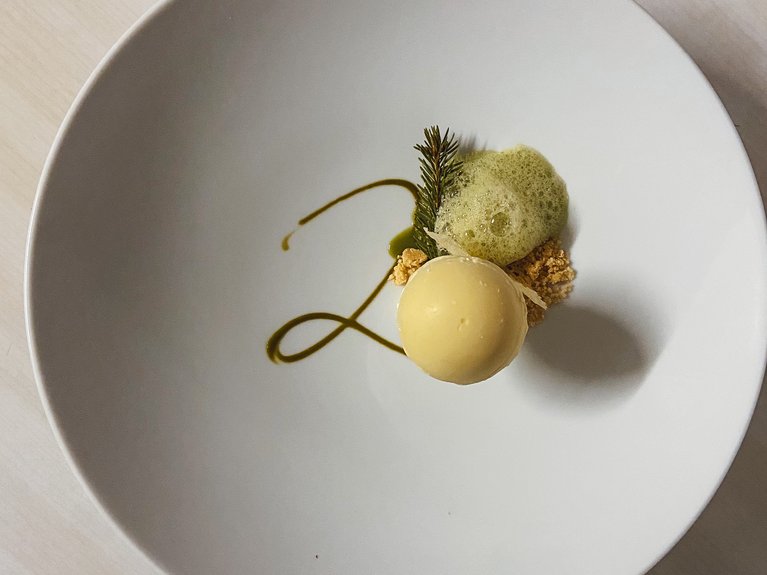 Hotel Latemar mit Dolomitenblick Gourmet-Dessert mit runder Mousse, grüner Dekoration und Schaum auf weißem Teller