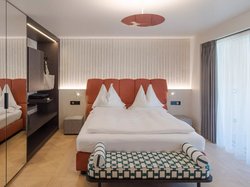 Hotel Latemar mit Dolomitenblick Modernes Schlafzimmer mit orangefarbenem Bett und gemusterter Bank davor