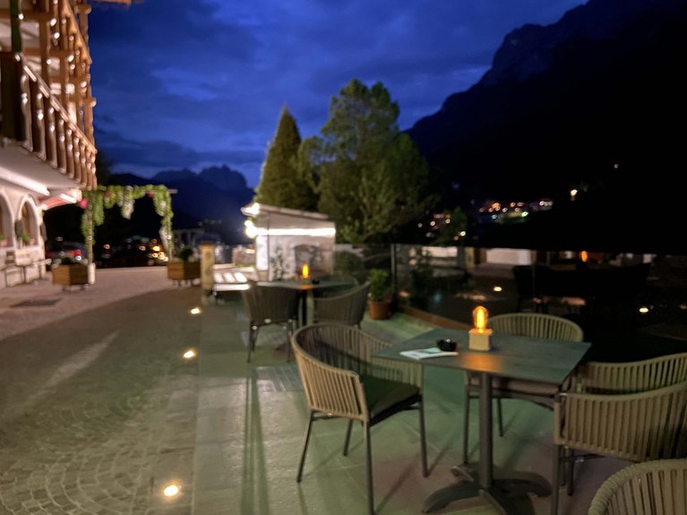 Hotel Latemar mit Dolomitenblick Abendliche Terrasse mit Tischen und Stühlen neben Gebäude und Bäumen beleuchtet