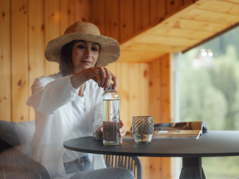 Hotel Latemar mit Dolomitenblick Frau mit Hut gießt Wasser aus Flasche auf einen Tisch