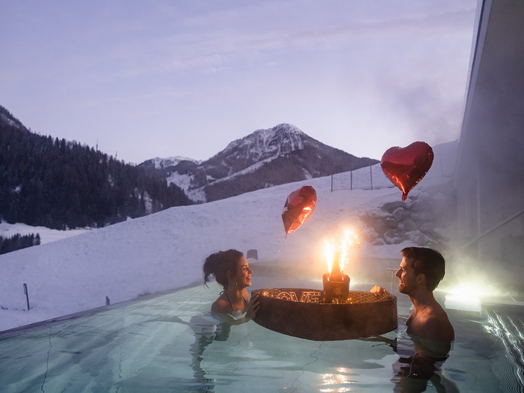 Hotel Latemar mit Dolomitenblick Paar im beheizten Pool mit schneebedecktem Berg und herzförmigen Ballons