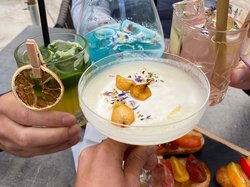 Hotel Latemar mit Dolomitenblick Vier Personen stoßen mit bunten Cocktails und Vorspeisen am Außentisch an