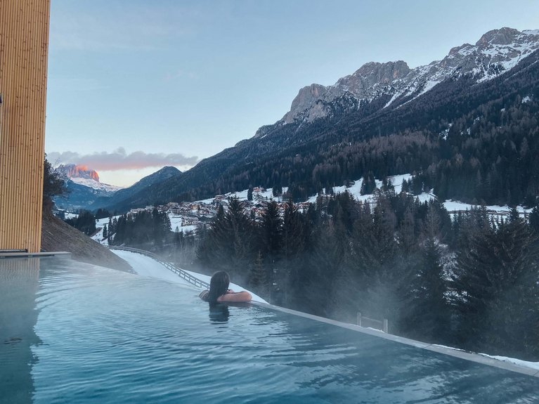 Hotel Latemar mit Dolomitenblick Person genießt einen Infinity-Pool mit Blick auf verschneite Berge und Dorf