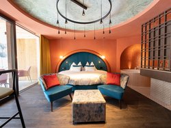 Hotel Latemar mit Dolomitenblick Modernes Schlafzimmer mit blauen Sesseln, rundem Bett und großem Fenster
