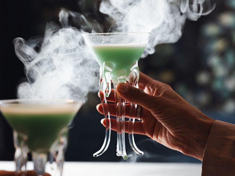 Hotel Latemar mit Dolomitenblick Hände halten Gläser mit grünem rauchendem Cocktail