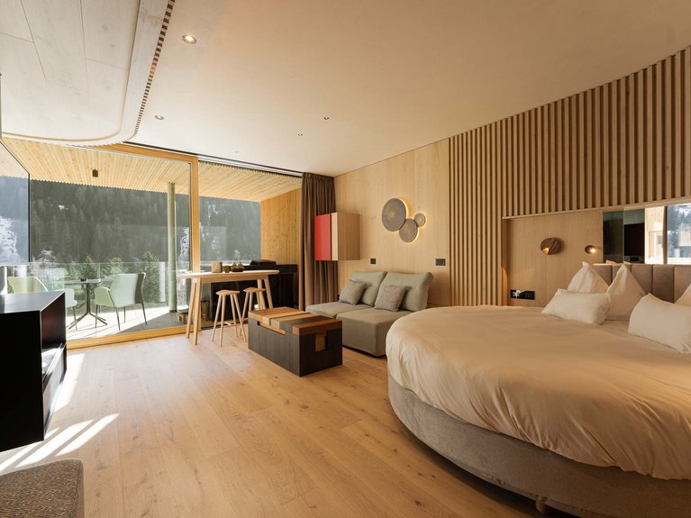 Hotel Latemar mit Dolomitenblick Modernes Zimmer mit rundem Bett, Sofa, TV und Balkon mit Bergblick