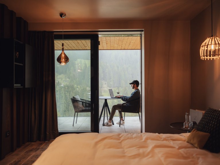 Hotel Latemar mit Dolomitenblick Mann mit Mütze arbeitet am Laptop auf dem Balkon eines Hotelzimmers