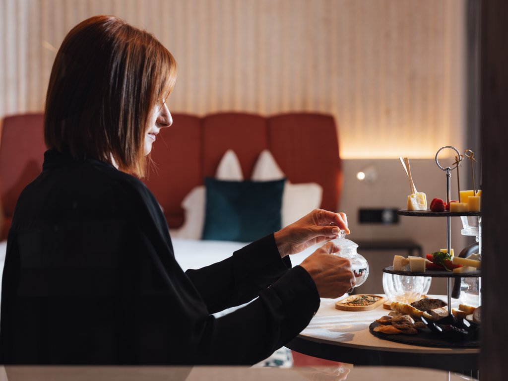 Hotel Latemar mit Dolomitenblick Frau öffnet ein Glas neben einem Tisch mit Essen in einem Schlafzimmer