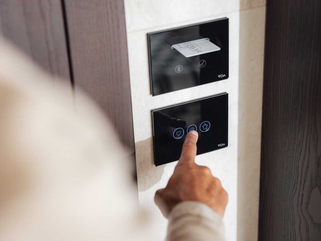 Hotel Latemar mit Dolomitenblick Person drückt einen Touchknopf auf einem schwarzen Wandbedienfeld.