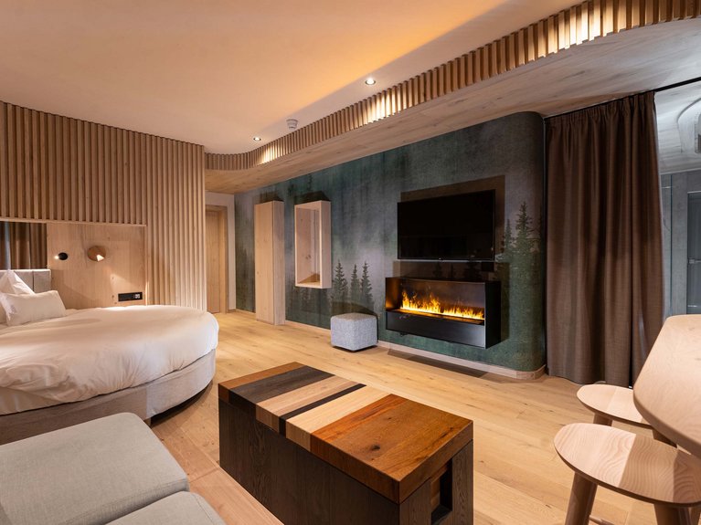 Hotel Latemar mit Dolomitenblick Modernes Hotelzimmer mit rundem Bett, elektrischem Kamin und Holzmöbeln