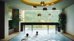 Hotel Latemar mit Dolomitenblick Innenpool mit zwei Personen und Bergblick durch ein großes Fenster