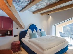 Hotel Latemar mit Dolomitenblick Modernes Schlafzimmer mit blauem Bett, Holzbalken und großem Fenster