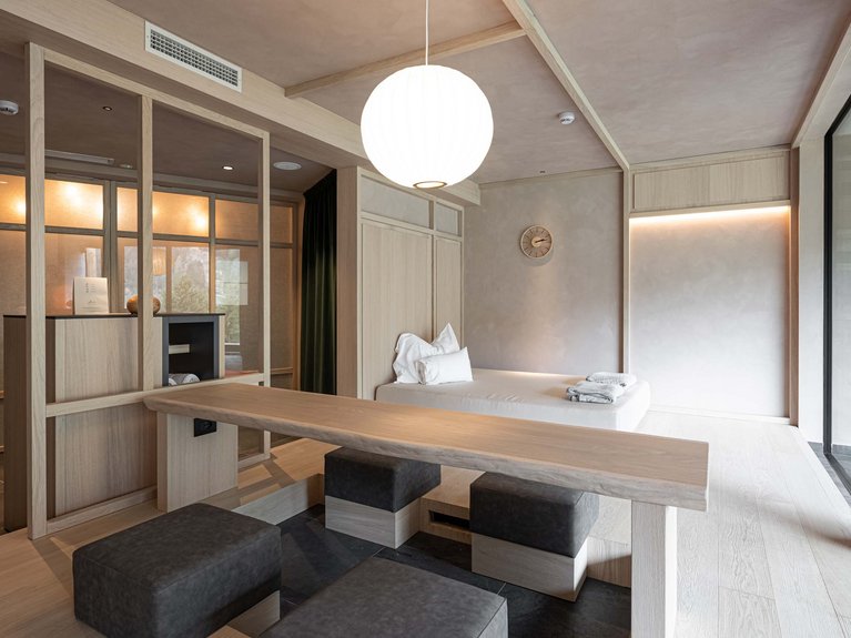 Hotel Latemar mit Dolomitenblick Modernes Zimmer mit weißer Liege, Holztisch und schwarzen Sitzwürfeln
