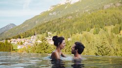 Hotel Latemar mit Dolomitenblick Glückliches Paar im Infinity-Pool mit Bergblick und Dorf unter blauem Himmel