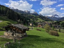 Hotel Latemar mit Dolomitenblick Holzhütte auf grünem Hügel mit Dorf und schneebedeckten Bergen im Hintergrund