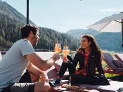 Hotel Latemar mit Dolomitenblick Paar sitzt im Freien und stößt mit Cocktails vor Bergkulisse an