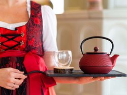 Hotel Latemar mit Dolomitenblick Frau in traditioneller Kleidung trägt Tablett mit roter Teekanne und Glas