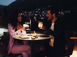 Hotel Latemar mit Dolomitenblick Paar stößt mit Cocktails bei einem Abendessen im Freien in gedämpftem Licht an.