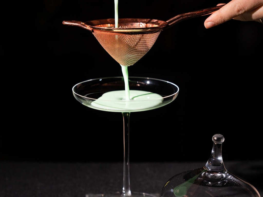 Per buongustai: l’hotel ideale vicino a Moena Cocktail verde viene filtrato in un bicchiere da cocktail su sfondo nero