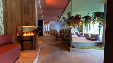 Meteo, Moena, Soraga, Latemar: tutto nella nostra gallery Interno di una spa con caminetto, divano rosso e lettini relax con piante appese.