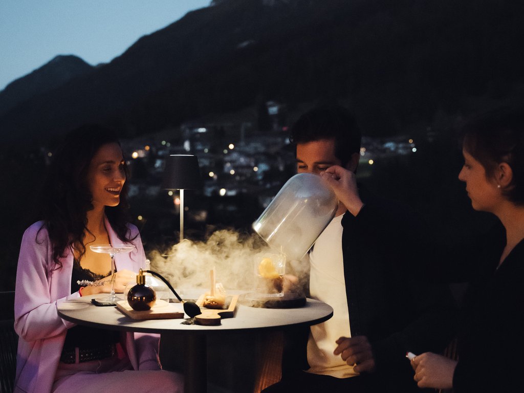 Sulla pista ciclabile, da Moena alla vostra oasi romantica Persone che godono di cocktail fumanti su una terrazza notturna in montagna