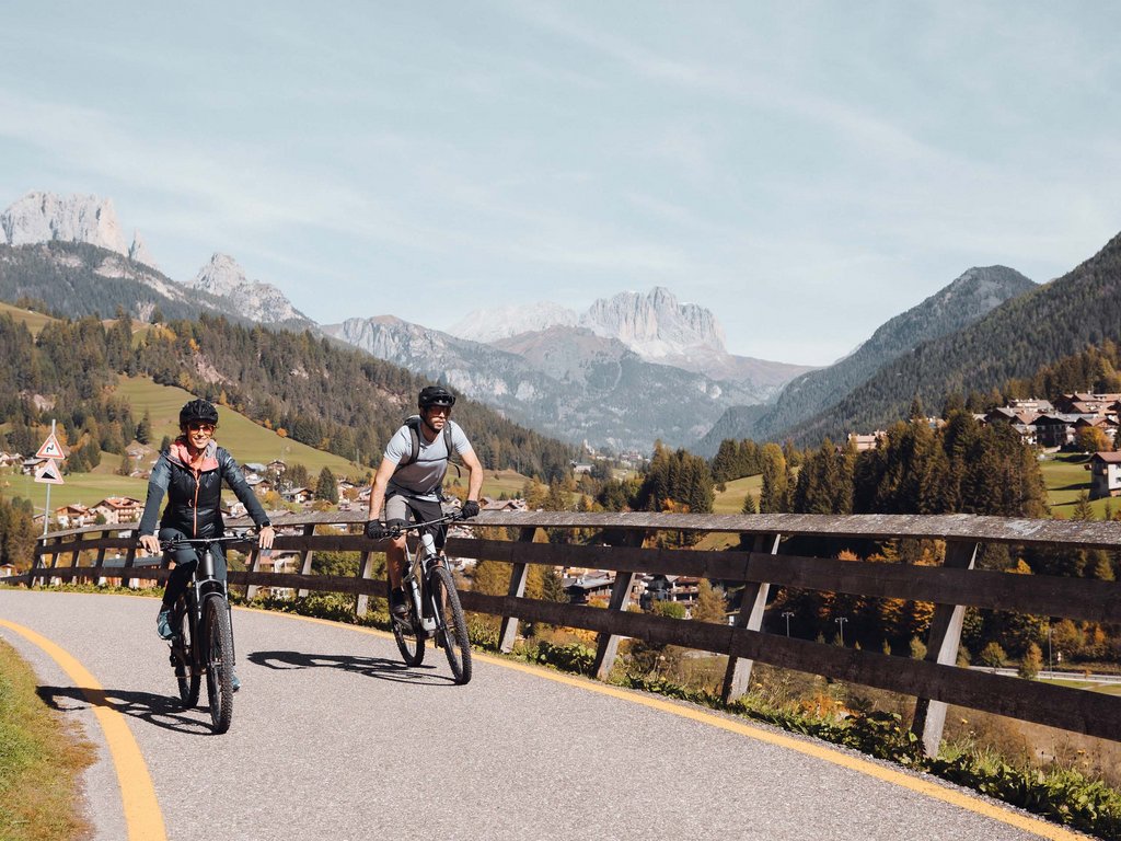 Lago di Soraga and summer activities near Hotel Latemar Two people cycling on a sunny mountain road with alpine scenery