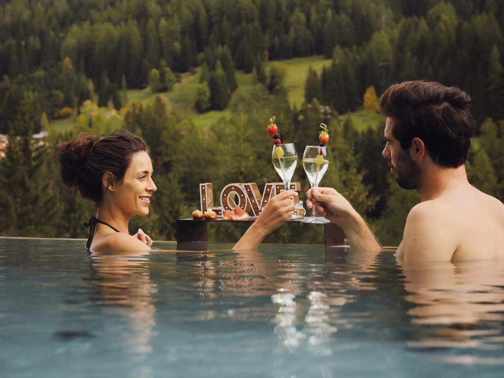 Hotel a Soraga di Fassa: benvenuti al Latemar Coppia si brinda in piscina con vista sulle montagne