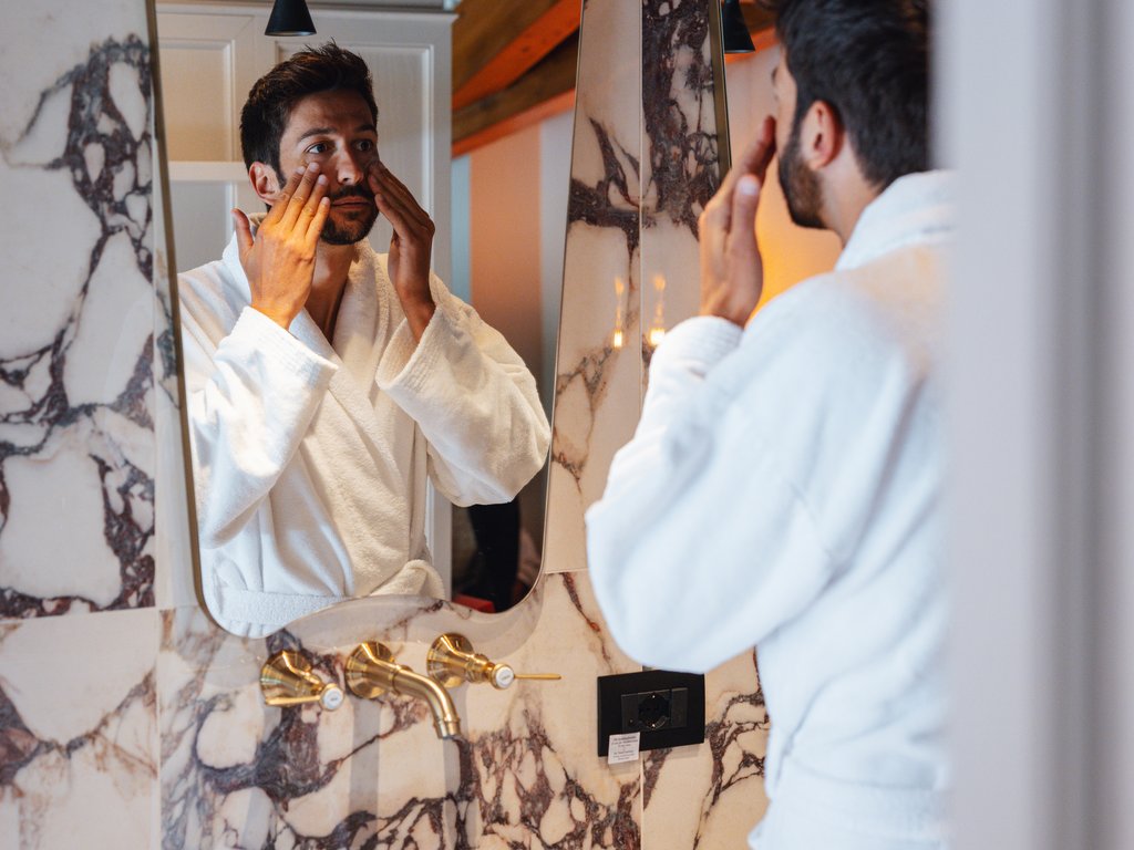 Soraga: dal lago alla piscina del Latemar Uomo in accappatoio che si cura il viso davanti allo specchio in bagno