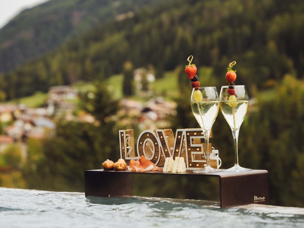 Dalla webcam il Latemar è bello, ma dal vivo è un sogno! Vassoio con snack e bicchieri con frutta in piscina con montagne sullo sfondo