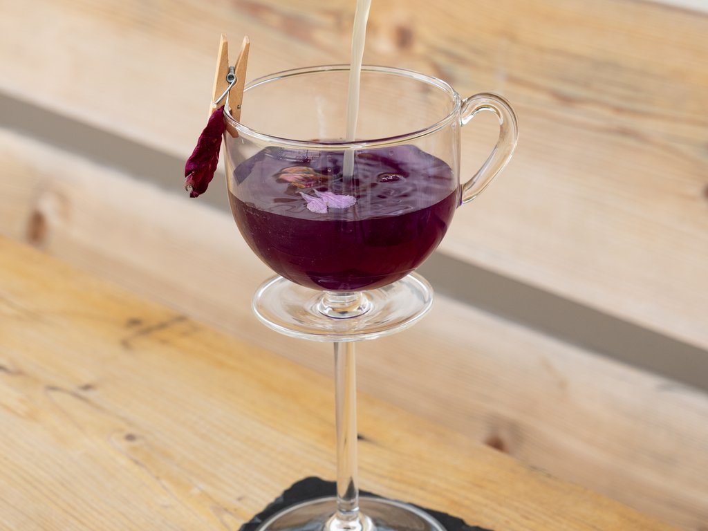 Val di Fassa and cycle track: outside our cocktail & tea bar Pouring clear liquid into glass with purple drink and flower petal