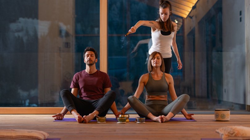 Val di Fassa: wandern, biken, erleben Zwei Personen meditieren, während eine dritte eine Räucherzeremonie in einem Raum durchführt