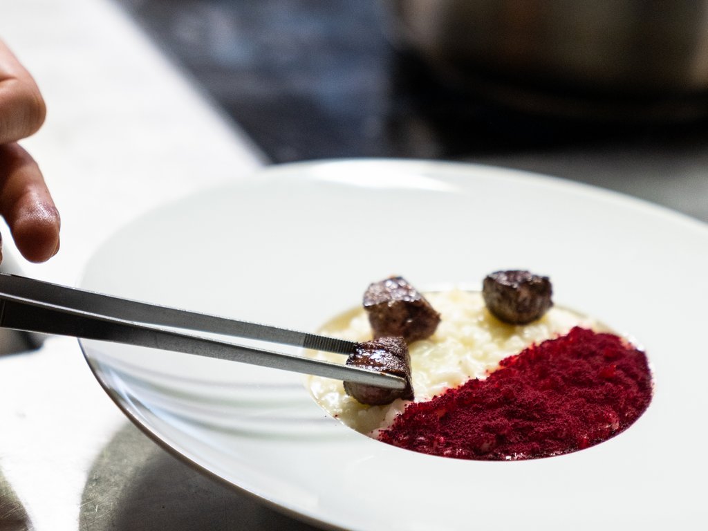 Per buongustai: l’hotel ideale vicino a Moena Chef sistema cubetti di carne su piatto creativo con crema e polvere rossa