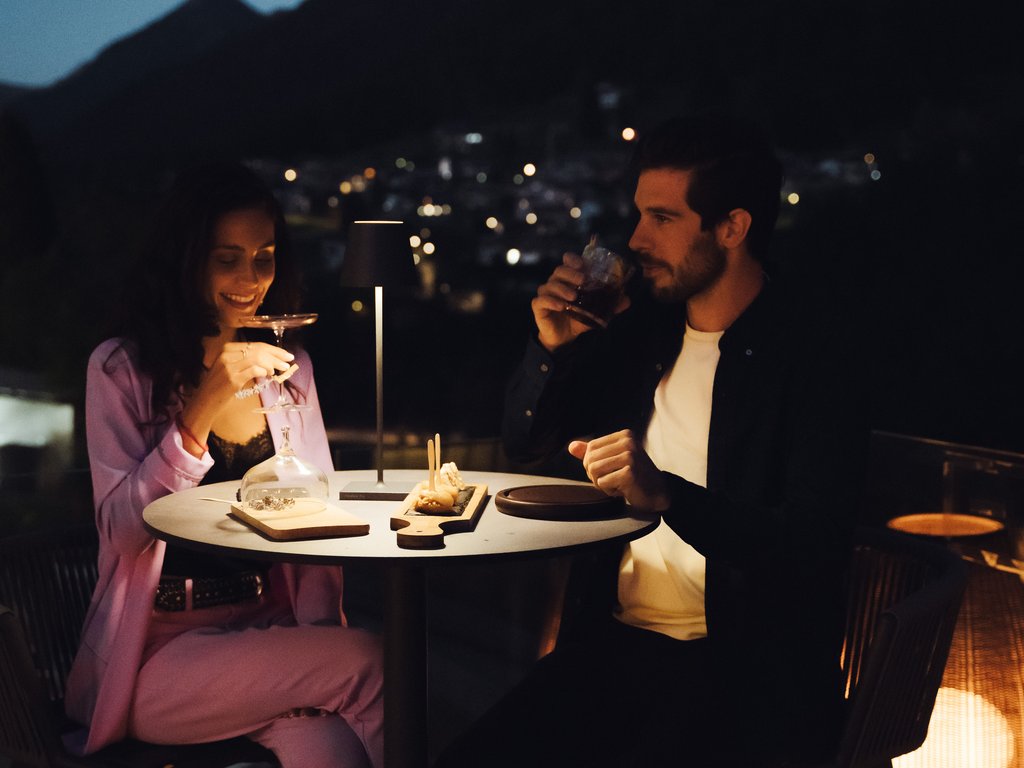 Sulla pista ciclabile, da Moena alla vostra oasi romantica Coppia che cena e beve su una terrazza romantica di sera con montagne sullo sfondo