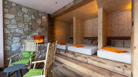 Meteo, Moena, Soraga, Latemar: tutto nella nostra gallery Area relax con lettini in legno, camino acceso e sedie con cuscini verdi