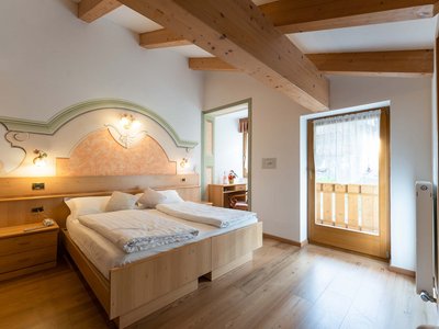 4-star Hotel in Soraga in Val di Fassa: rooms and suites Bedroom with double bed, wooden beam ceiling, and balcony