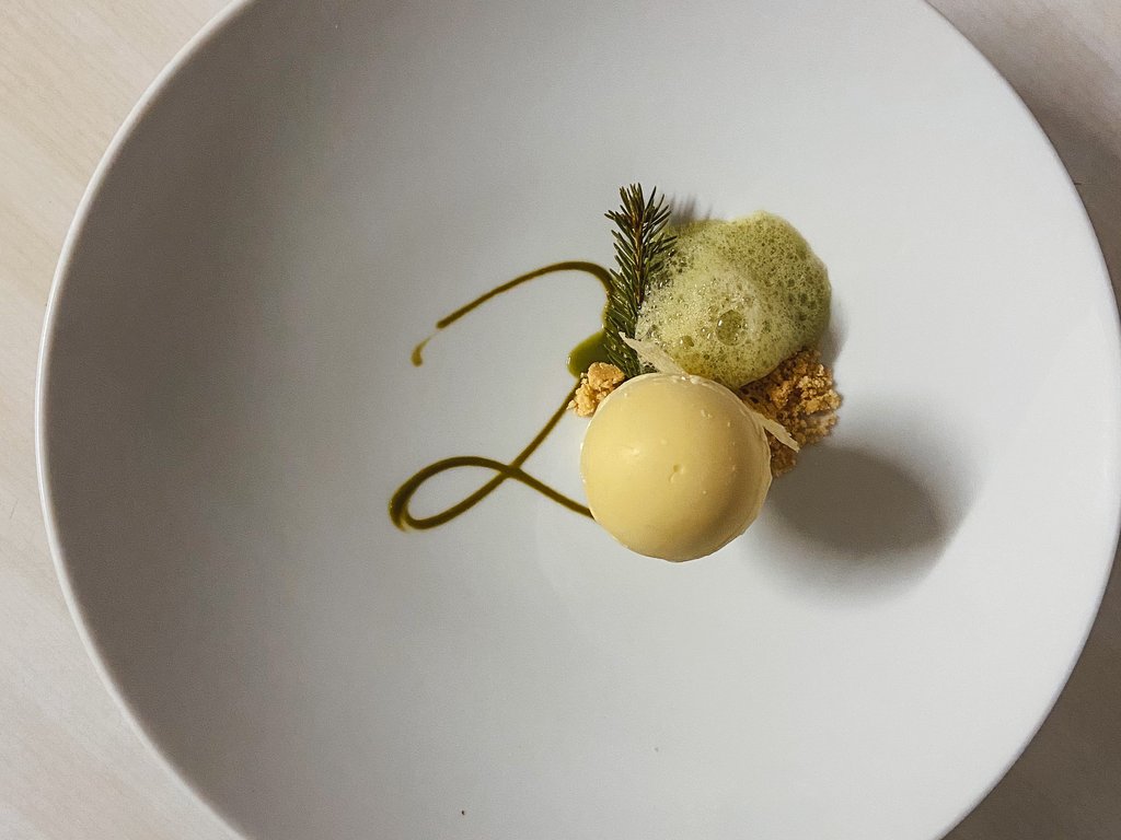 Val di Fassa: dove dormire e vivere vacanze sostenibili Dessert gourmet con mousse rotonda, decorazione verde e schiuma su piatto bianco