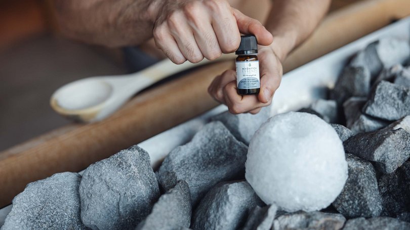 Val di Fassa: wandern, biken, erleben Hand hält eine kleine Flasche ätherisches Öl nahe Steinen und einem Eisstück