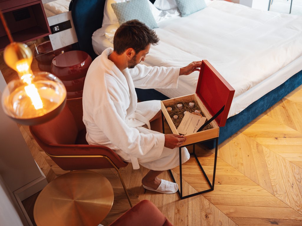 Soraga: dal lago alla piscina del Latemar Uomo in accappatoio che apre una scatola regalo in una stanza d'albergo