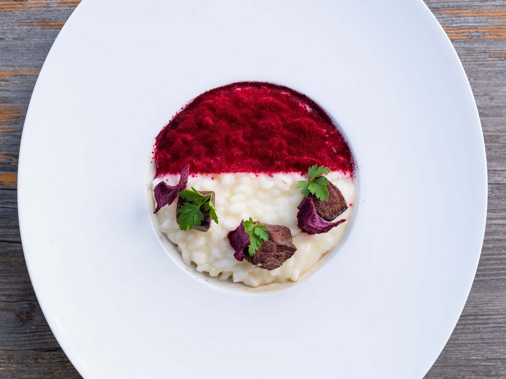 A Soraga il meteo è sempre ottimo per un Day Spa! Risotto cremoso con polvere rossa, carne e foglie verdi su piatto bianco