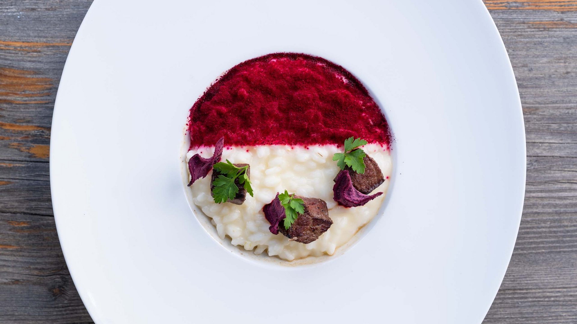Gourmetrestaurant im Val di Fassa: das Mirage Cremiges Risotto mit rotem Puder, Fleischstücken und grünen Blättern auf weißem Teller