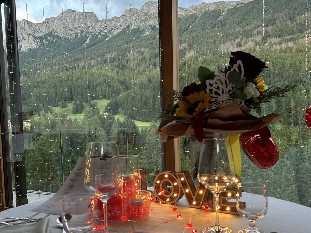 Sulla pista ciclabile, da Moena alla vostra oasi romantica Tavolo apparecchiato con decorazioni romantiche e vista sulle montagne dalla finestra