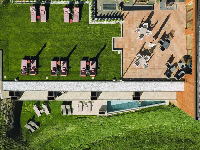 Hotel Latemar mit Dolomitenblick Luftaufnahme von Liegestühlen und Tischen auf Rasen und Terrasse eines modernen Gebäudes
