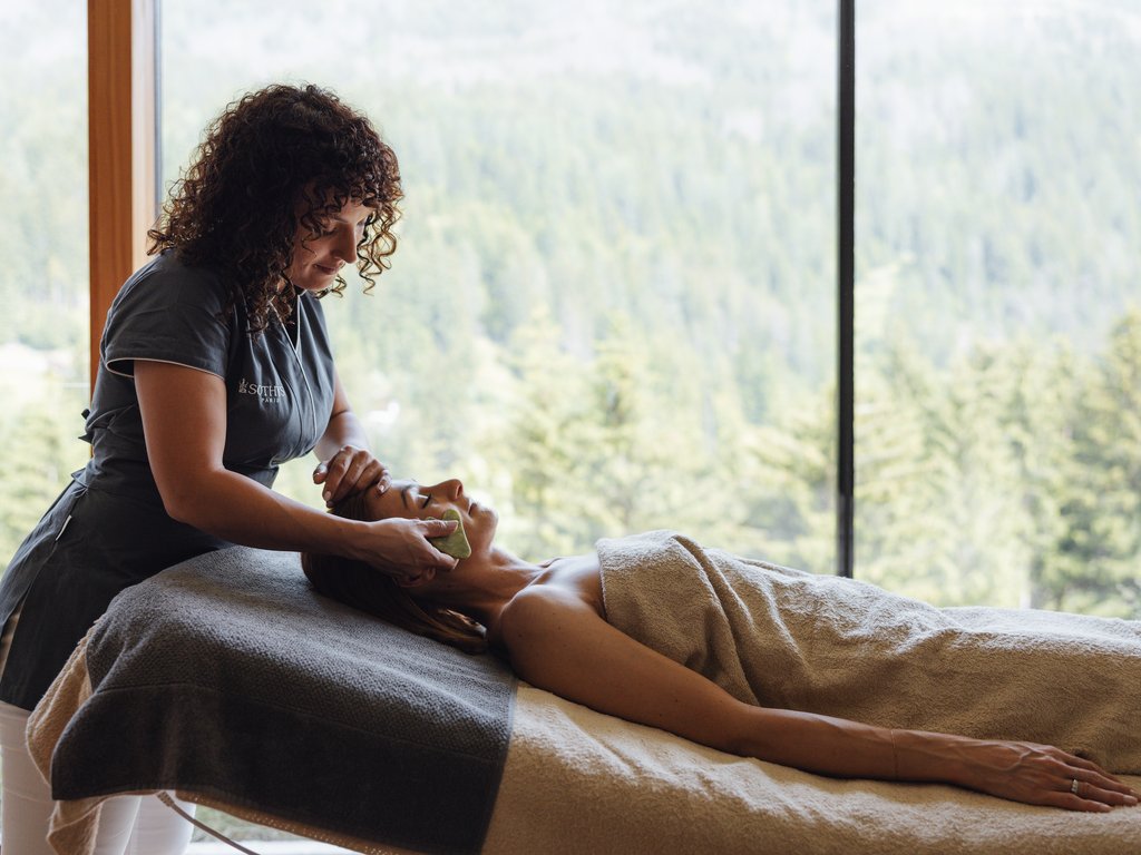 Trentino: Hotel am See mit Pool und Spa Masseurin führt Gesichtsbehandlung mit Stein bei Kunde im Spa durch