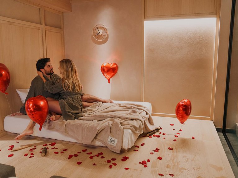 Urlaub im Fassatal: Erholung pur Romantisches Paar auf Bett mit herzförmigen Luftballons und roten Blütenblättern