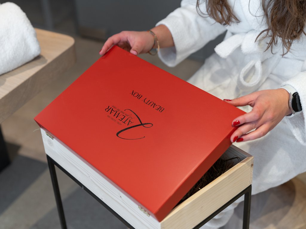 Soraga: dal lago alla piscina del Latemar Donna in accappatoio apre scatola rossa di bellezza su tavolino