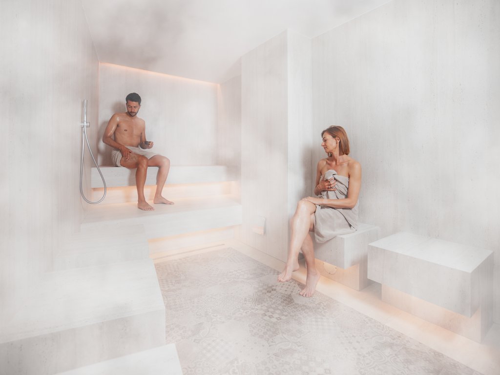 In Soraga, the weather is always right for a day spa! Man and woman relaxing seated in modern sauna with soft lighting