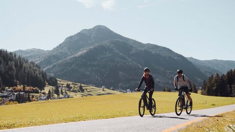 Picture gallery Two people cycling on a country road with mountains in the background
