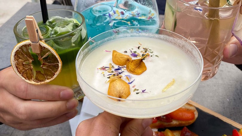 Val di Fassa: wandern, biken, erleben Vier Personen stoßen mit bunten Cocktails und Vorspeisen am Außentisch an